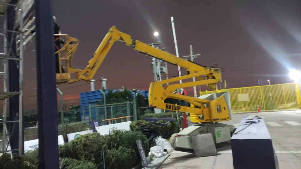 Plataforma de brazo articulado Haulotte HA151P trabajando de noche en instalación industrial Plataforma de brazo articulado Haulotte HA151P trabajando de noche en instalación industrial